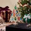 A sparkling rhinestone Christmas tree brooch pin with colorful gemstone leaves displayed on a black velvet surface.
