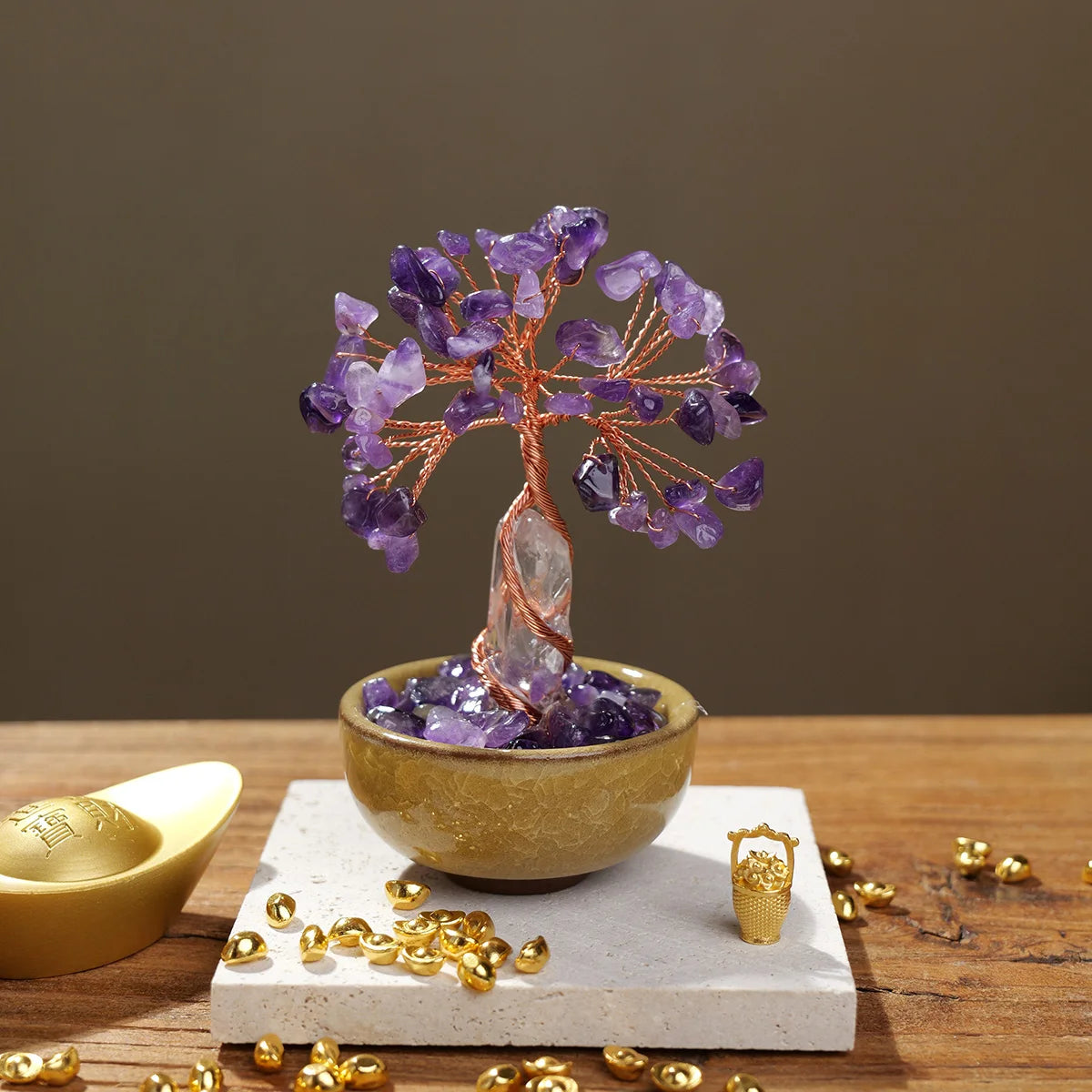 A natural crystal money tree with a rose quartz base sits on a light stone, surrounded by gold coins.