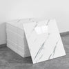 A stack of white marble peel-and-stick wall panels displaying gray veining on a gray concrete surface.