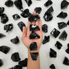 A hand holds several raw, black healing crystal stones against a white background.