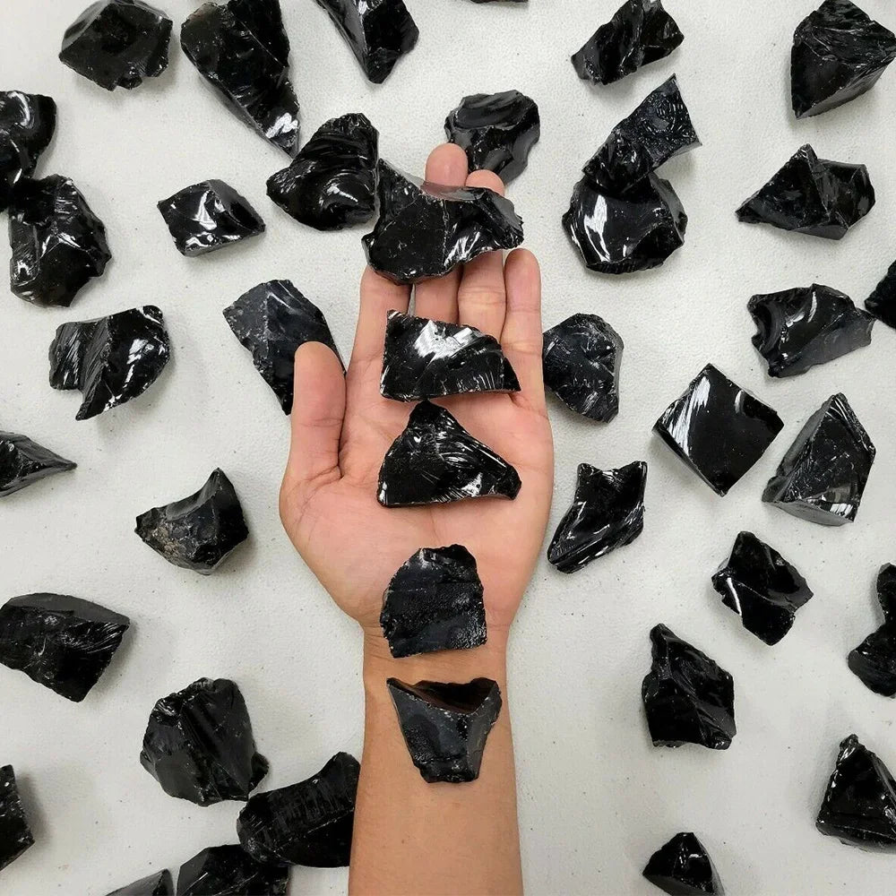 A hand holds several raw, black healing crystal stones against a white background.