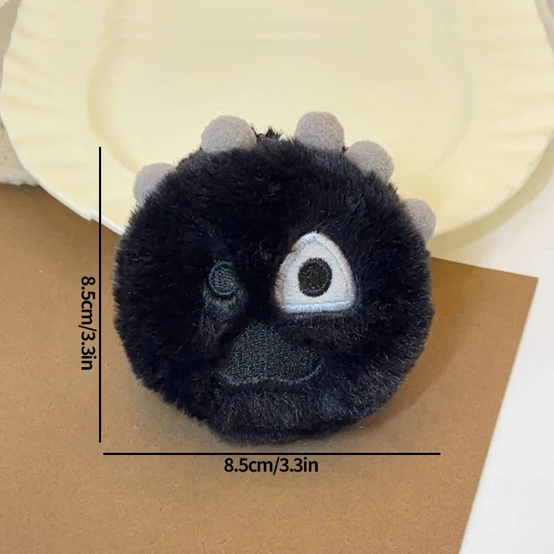 A black plush keychain with a clear eye and small spikes is shown against brown paper.