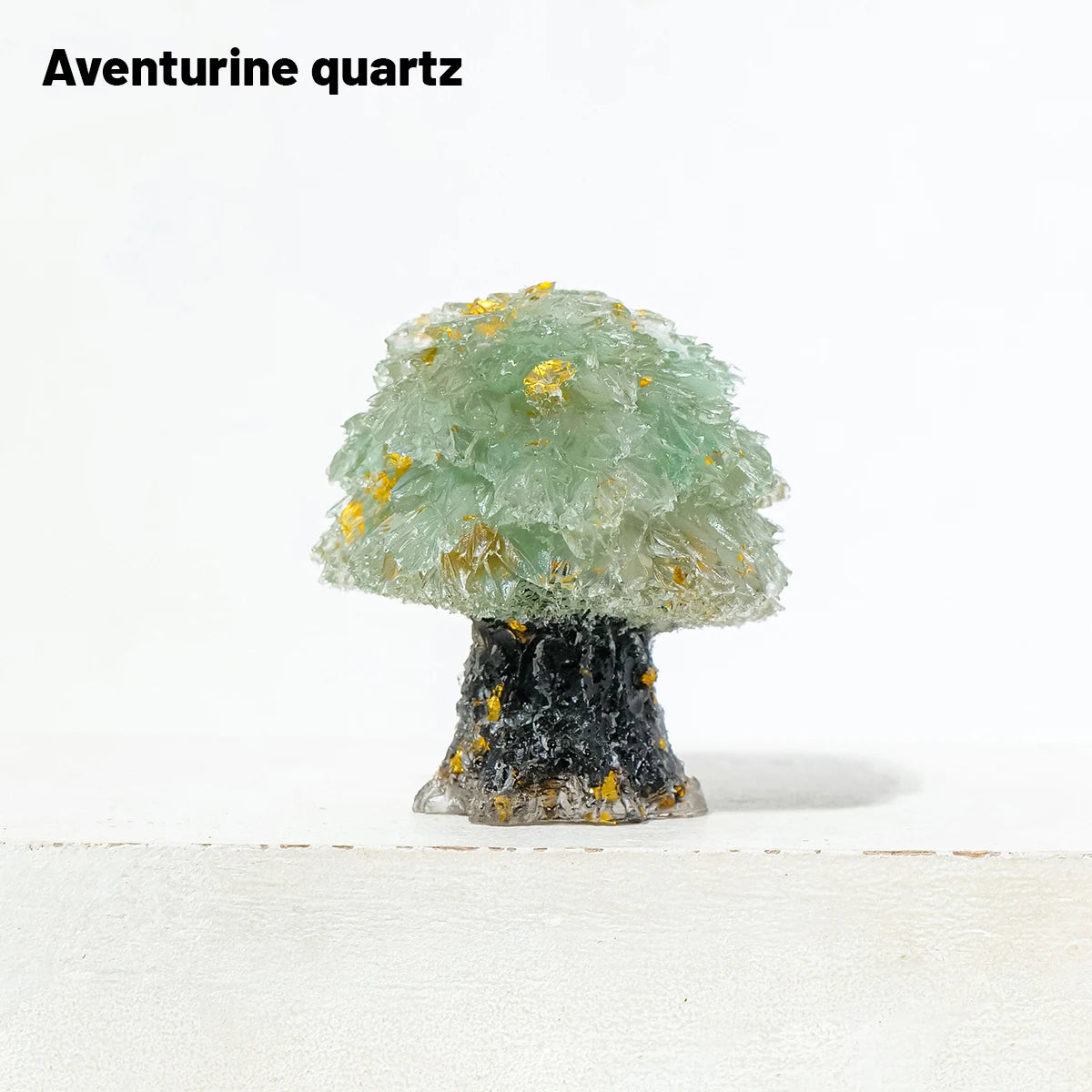 A natural Aventurine quartz crystal sculpture shaped like a tree with green foliage and gold accents atop a dark base.
