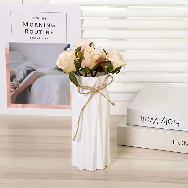 A white vase holds a bouquet of pink and cream roses on a wooden surface.