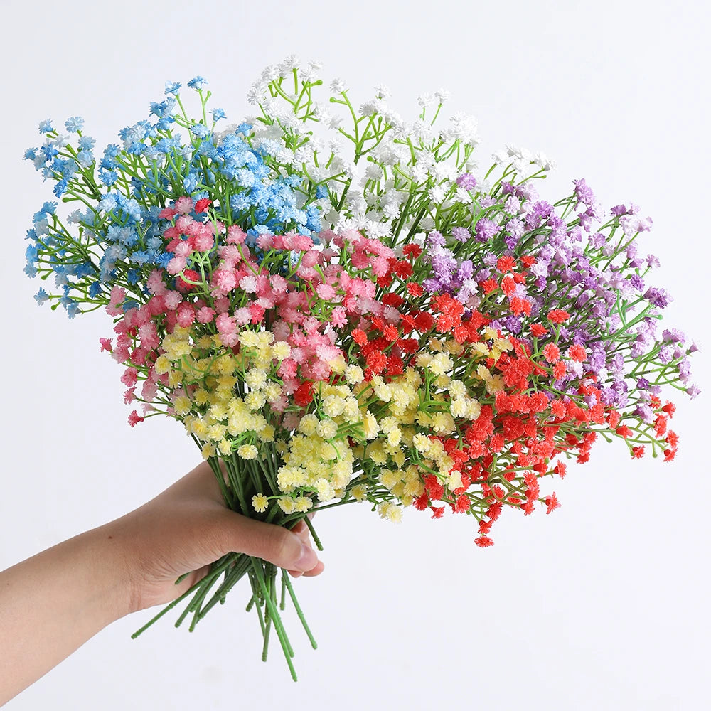 A hand holds a bouquet of artificial baby's breath flowers in various shades of blue, pink, white, and red.