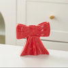 A bright red ceramic bow candle holder with a textured finish sits on a white surface.