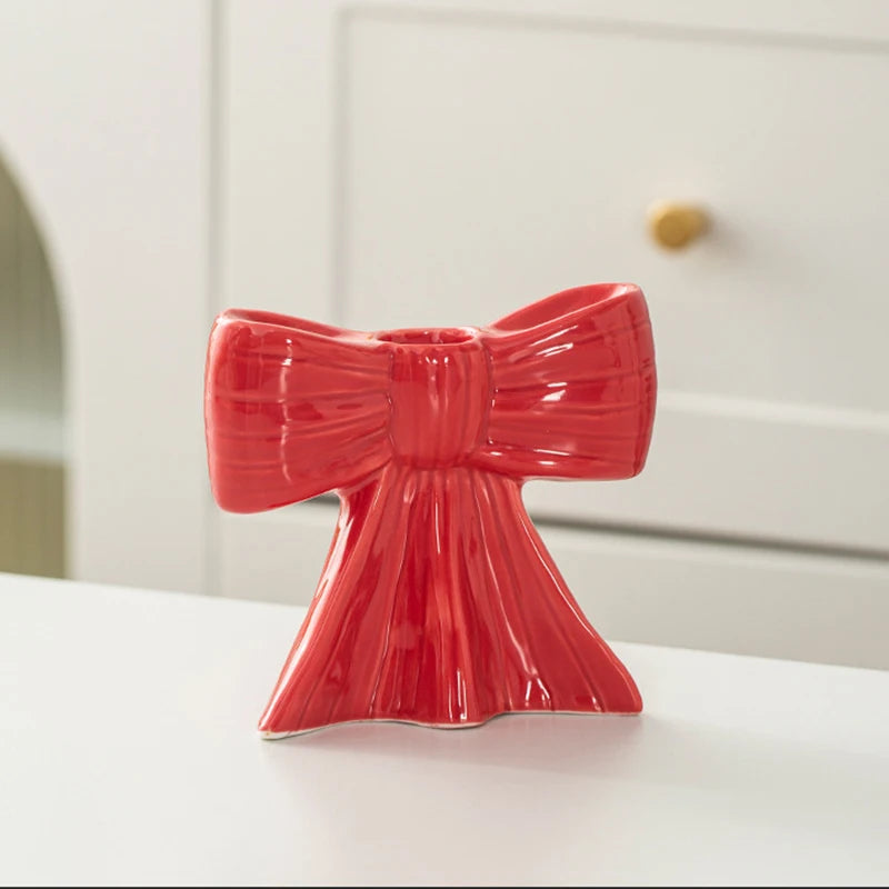 A bright red ceramic bow candle holder with a textured finish sits on a white surface.