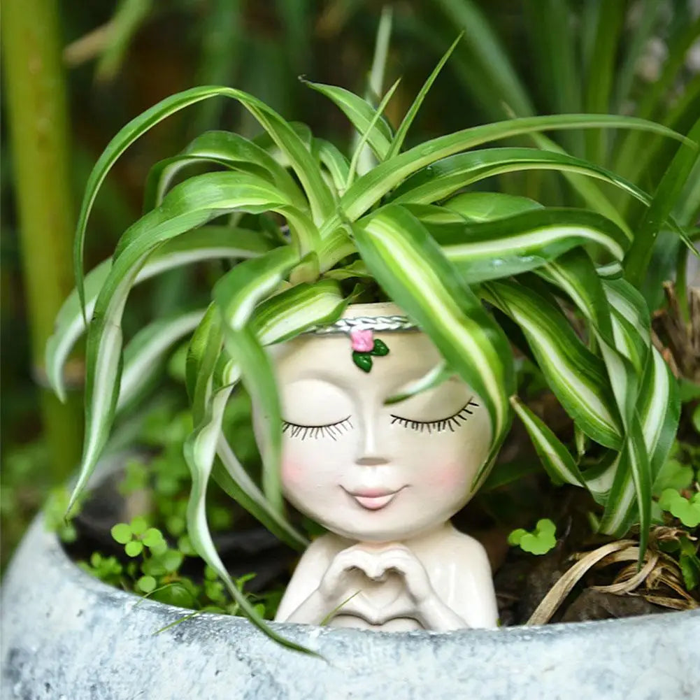 A white resin girl face planter with a drainage hole surrounded by green foliage.