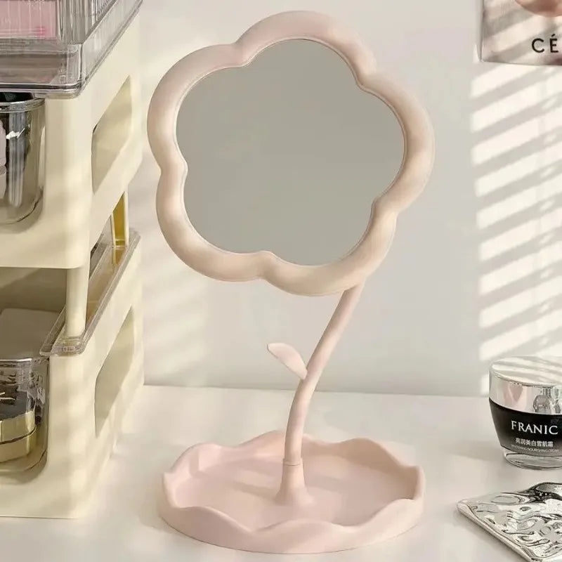 A pink floral decorative desktop mirror with a scalloped frame and stand is shown on a white surface.