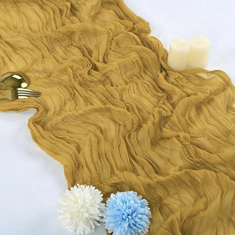 A golden beige gauze table runner with white candles and blue and white flowers.