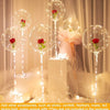 Clear bubble balloons with red roses and string lights displayed on a white pedestal.