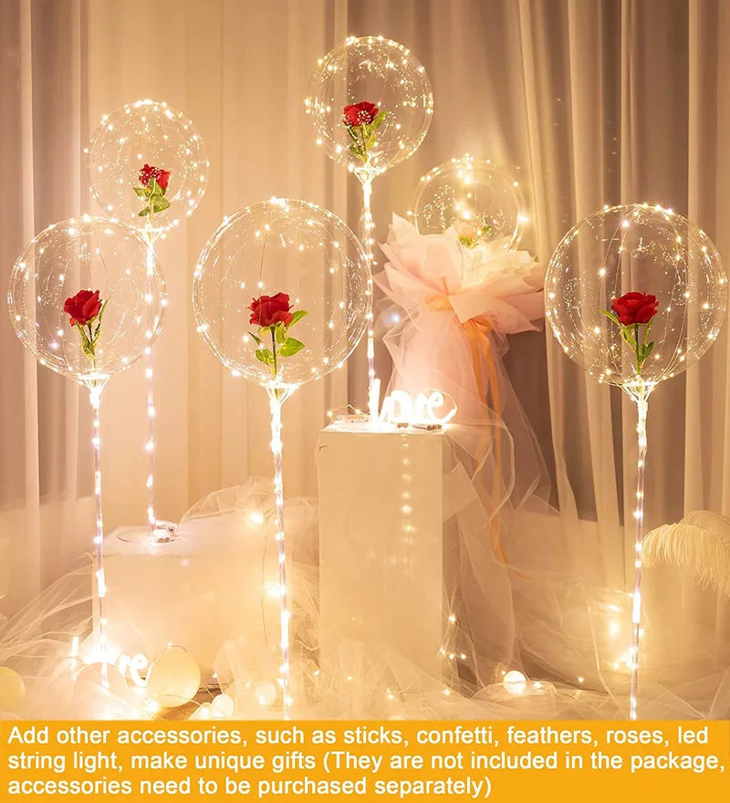 Clear bubble balloons with red roses and string lights displayed on a white pedestal.