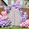 A large balloon arch decoration for a first birthday party featuring pink and purple balloons and a sign.