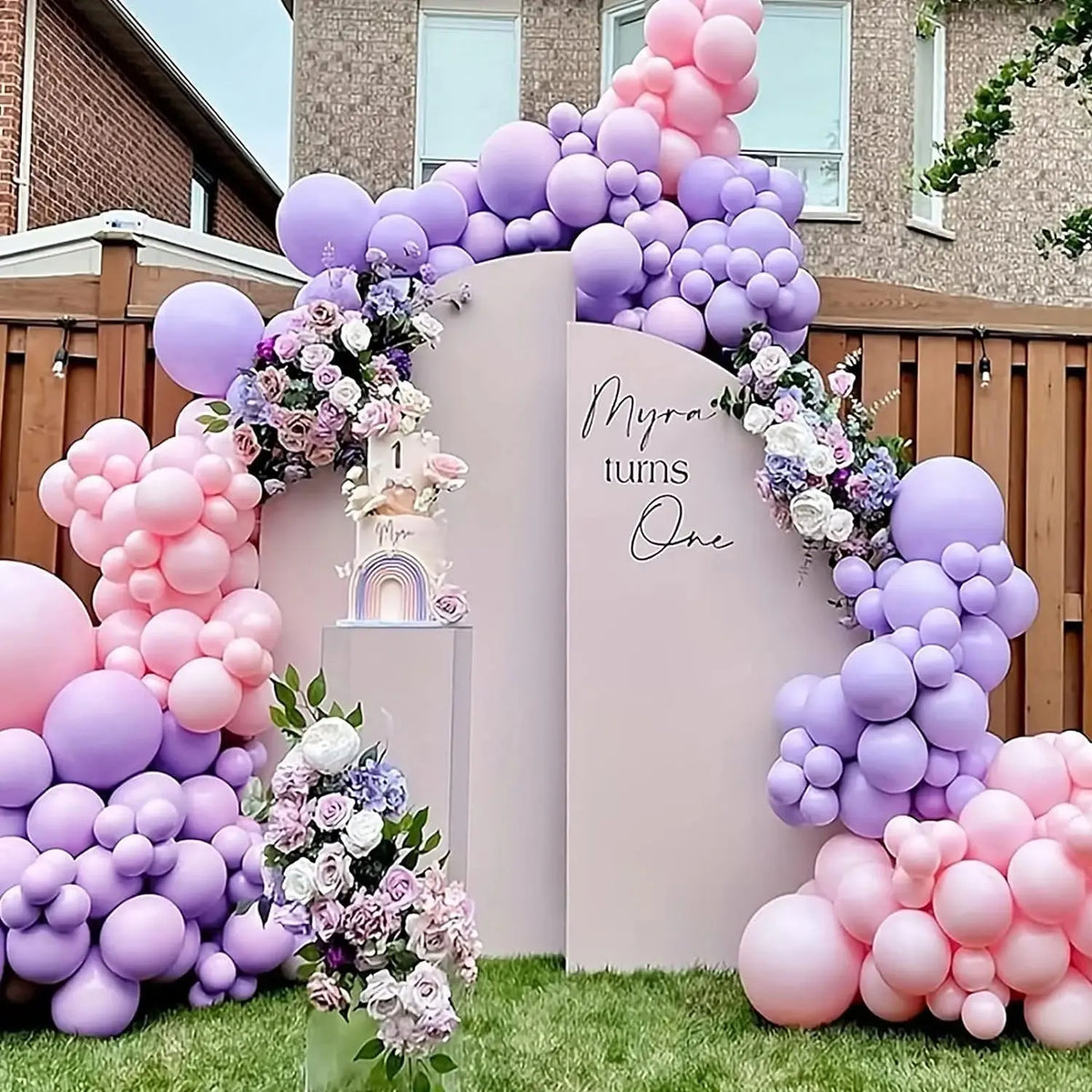 A large balloon arch decoration for a first birthday party featuring pink and purple balloons and a sign.
