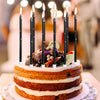 A tiered cake decorated with candles and fruit, featuring layers of light-colored frosting.