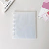 A clear, vertical transparent card organizer or notebook lies on a white surface next to a white tool.