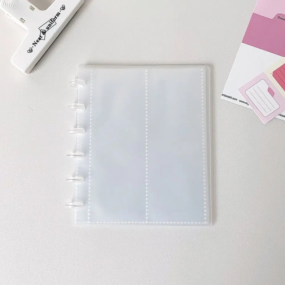 A clear, vertical transparent card organizer or notebook lies on a white surface next to a white tool.