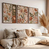 A set of three canvas art prints featuring sage green and earthy floral designs displayed on a white wall.