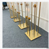 A row of tall gold metal candelabra with glass candle holders displayed on a gray carpet.