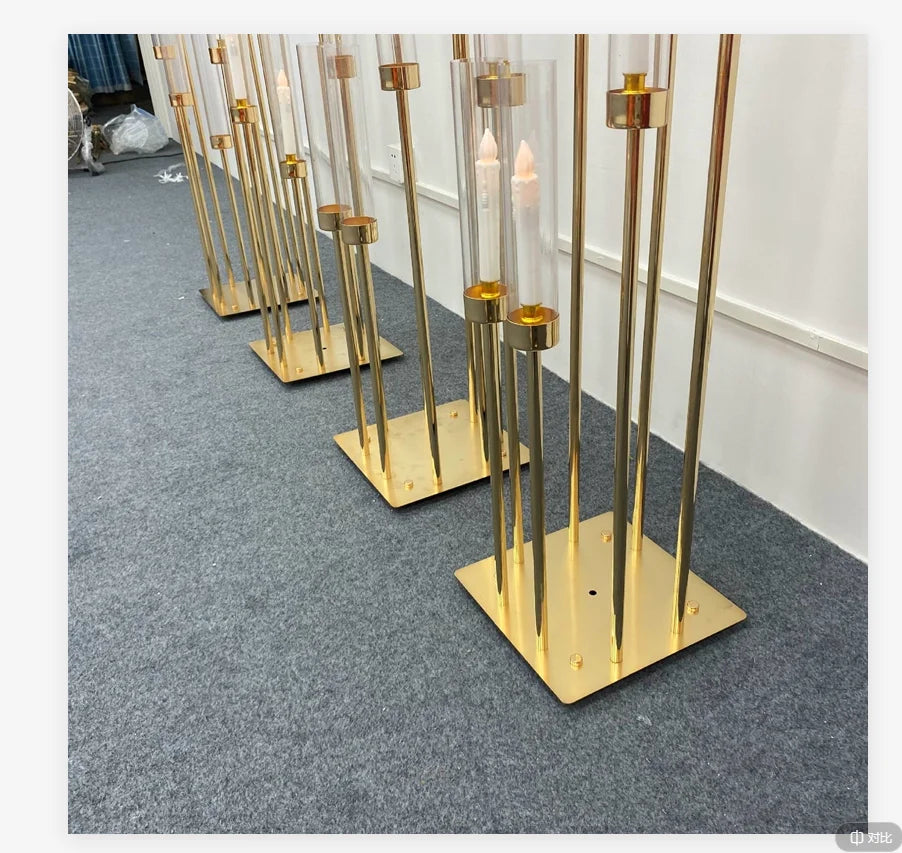 A row of tall gold metal candelabra with glass candle holders displayed on a gray carpet.