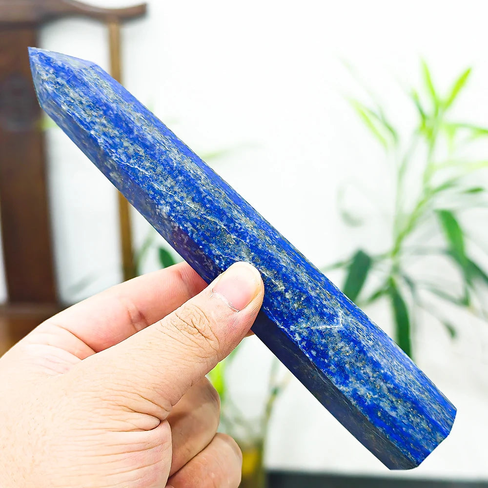 A hand holds a polished blue lapis lazuli crystal tower for meditation and home decor.