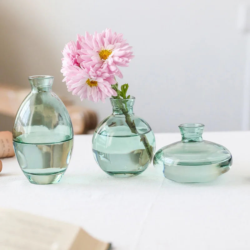 A set of three minimalist glass bud vases filled with water and featuring a pink flower.