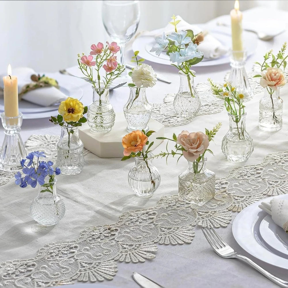 A table setting featuring diamond faceted glass bud vases with flowers and candles on a white linen tablecloth.