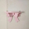 A pink decorative bow-shaped wooden wall shelf mounted on a white wall.