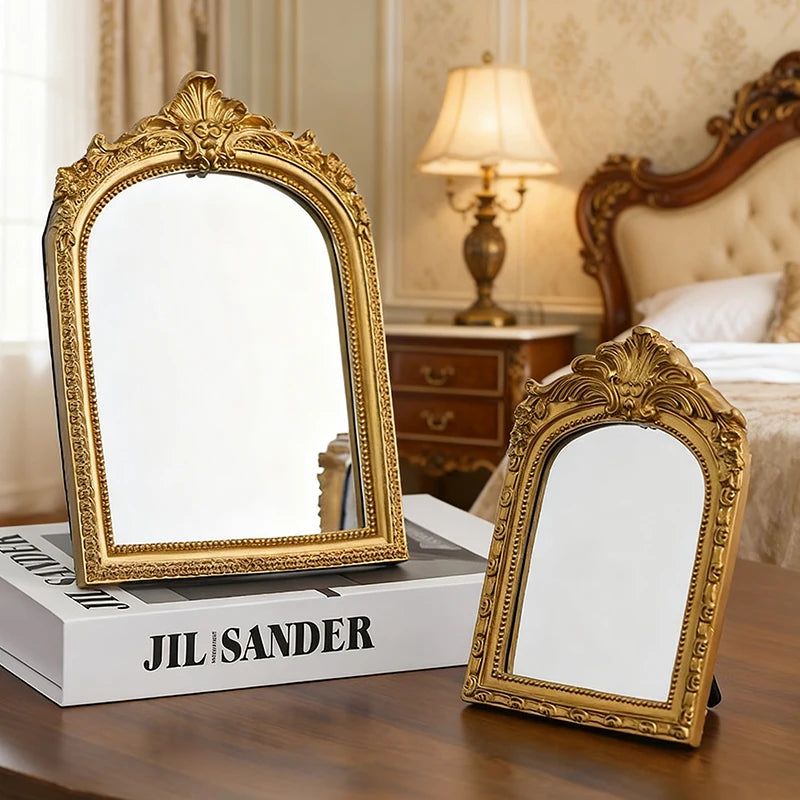 A vintage gold-framed arched vanity mirror resting on a wooden table.
