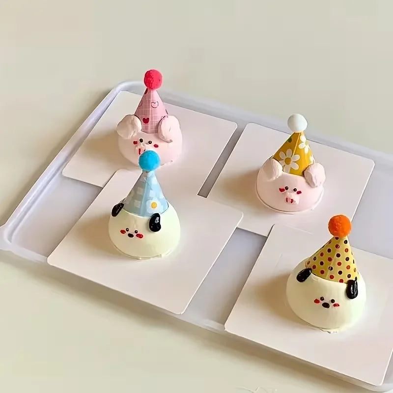 Three pink and yellow animal-themed party hat cake toppers displayed on a white rectangular platter.