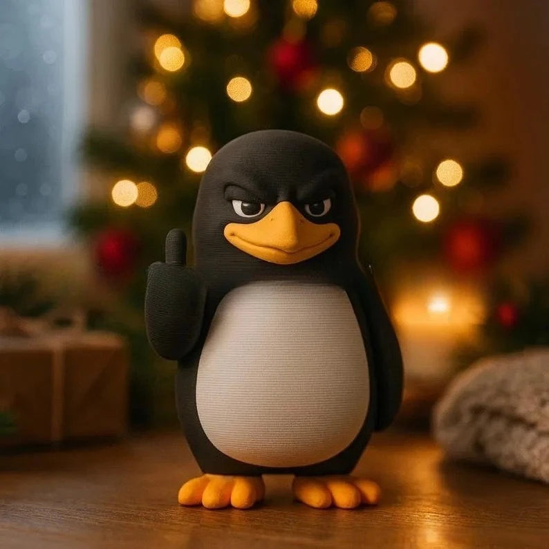 A black and white penguin desk statue with a raised flipper sitting on a wooden surface in front of a blurred Christmas tree.