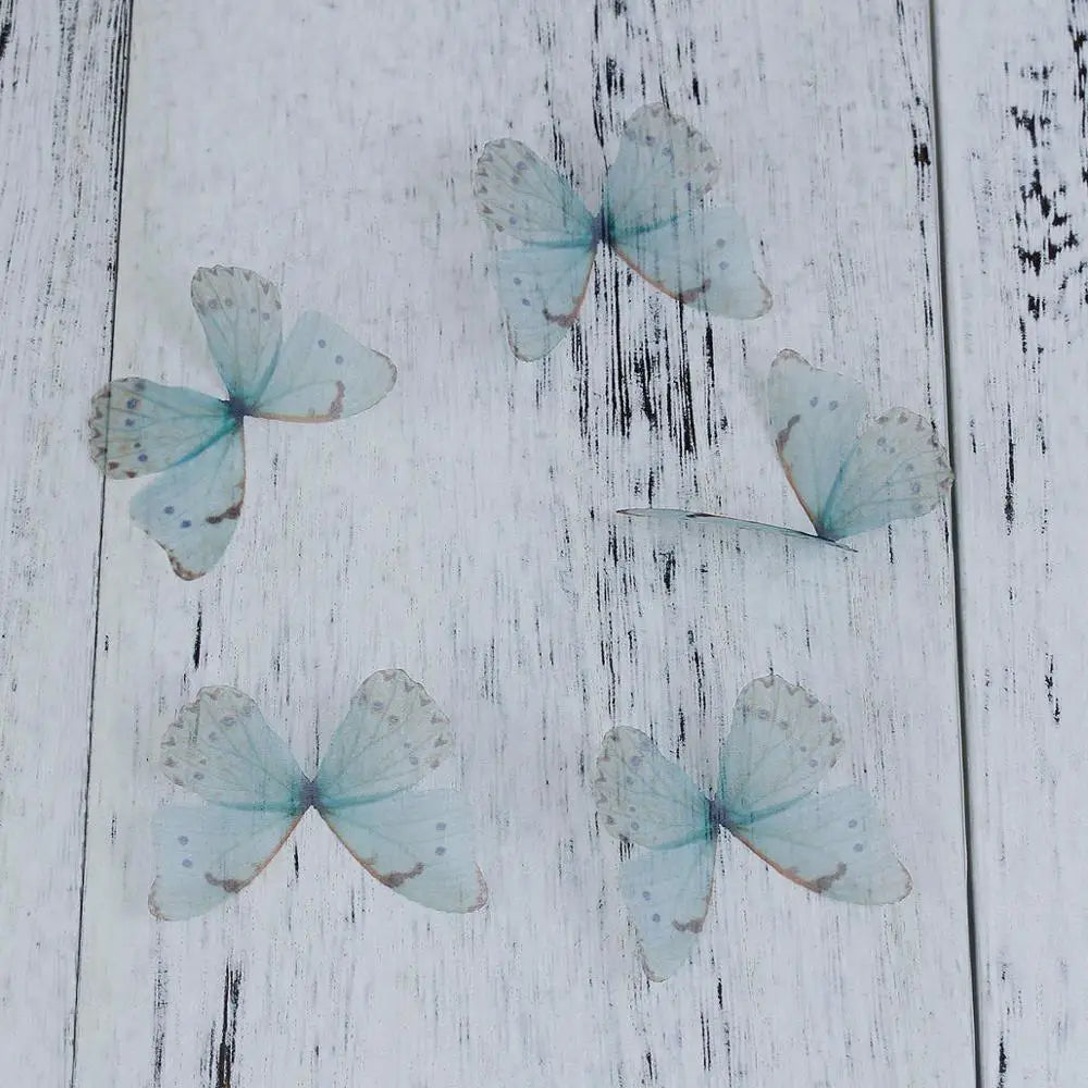 Four light blue organza butterfly embellishments scattered on a white wooden surface.