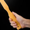A hand holds a light wood bamboo back scratcher with a roller massager against a black background.