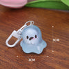A light blue glow-in-the-dark ghost keychain with a white loop and measurements shown on a wooden surface.