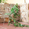 A white metal trellis with artificial ivy vines growing against a stacked stone wall.