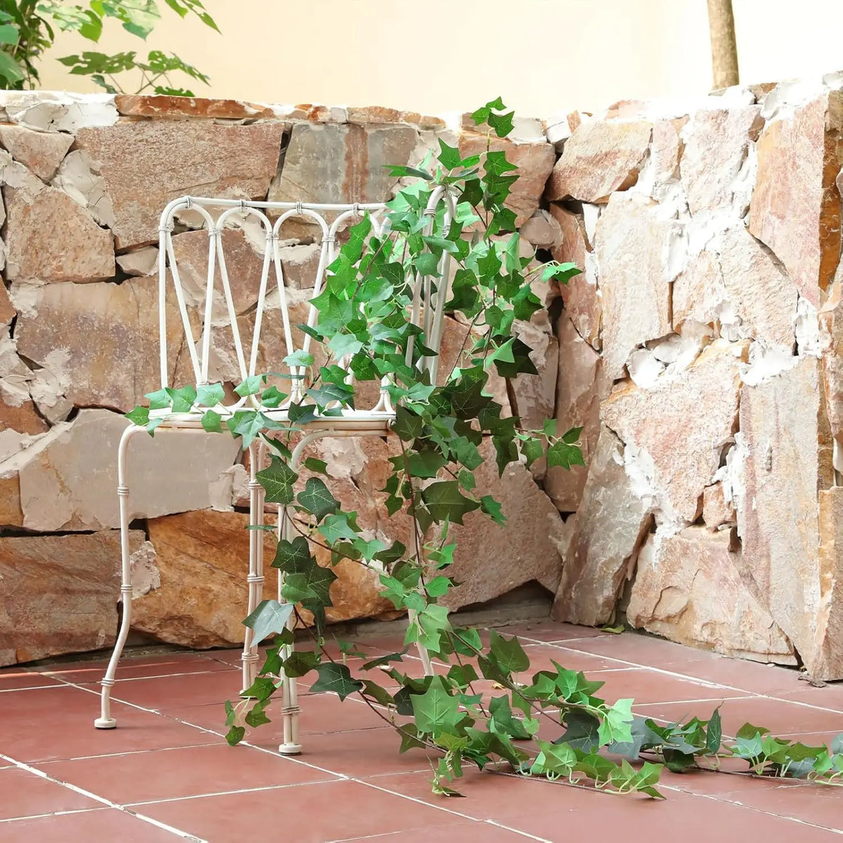 A white metal trellis with artificial ivy vines growing against a stacked stone wall.