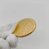 A hand holds a gold commemorative iron coin with an embossed design against a white background.