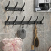 Percha de pared robusta negra con seis ganchos montados en una pared de azulejos, con varios artículos colgados.