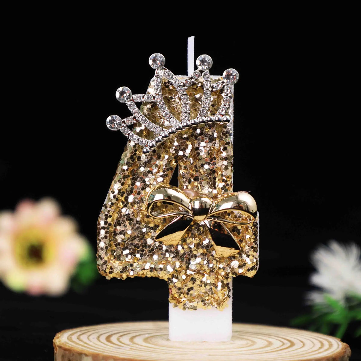 Gold glitter number 4 cake topper candle with a rhinestone bow on a wooden slice.