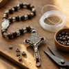A silver crucifix pendant with a red enamel finish rests on a wooden surface next to beaded bracelets and fishing line.
