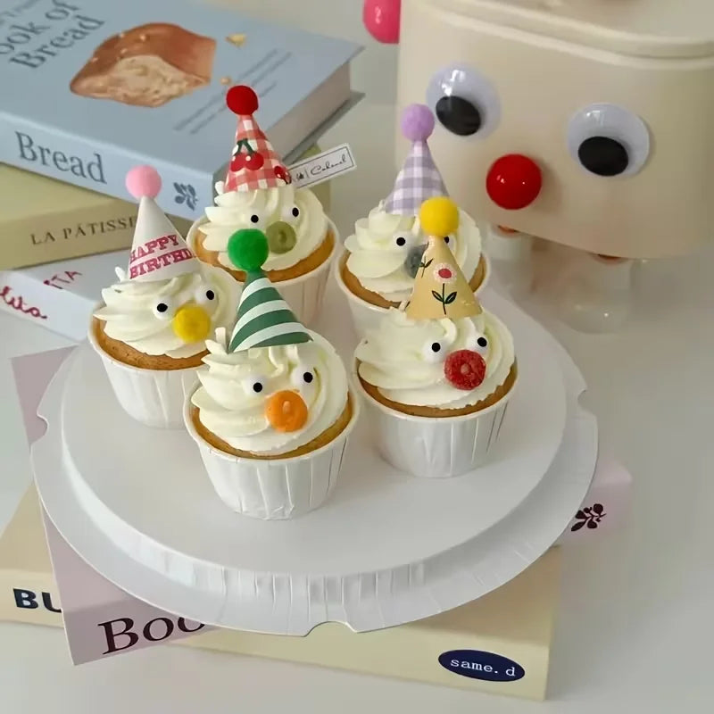 A set of three mini colorful party hat cake toppers displayed on a white cake stand.