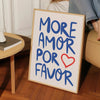A framed canvas print featuring the text MORE AMOR FOR FAVOR in blue script on a light background.