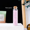 A glass bottle filled with pink rose quartz crystals sits on a white surface.