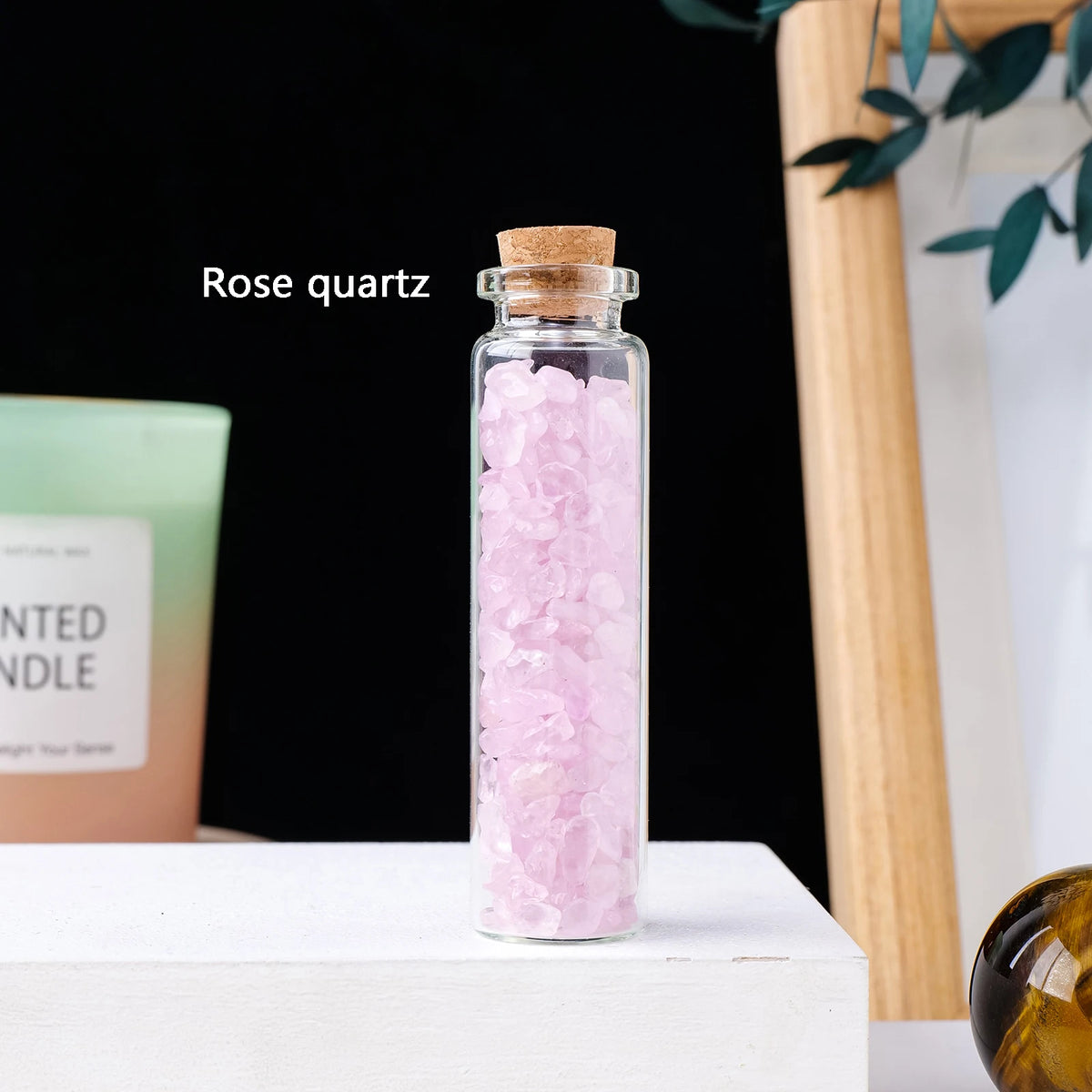 A glass bottle filled with pink rose quartz crystals sits on a white surface.