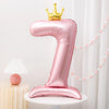 A pink foil balloon shaped like the number one with a gold crown on top.