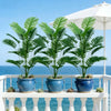 Three potted artificial palm trees with monstera leaves displayed on a white railing.
