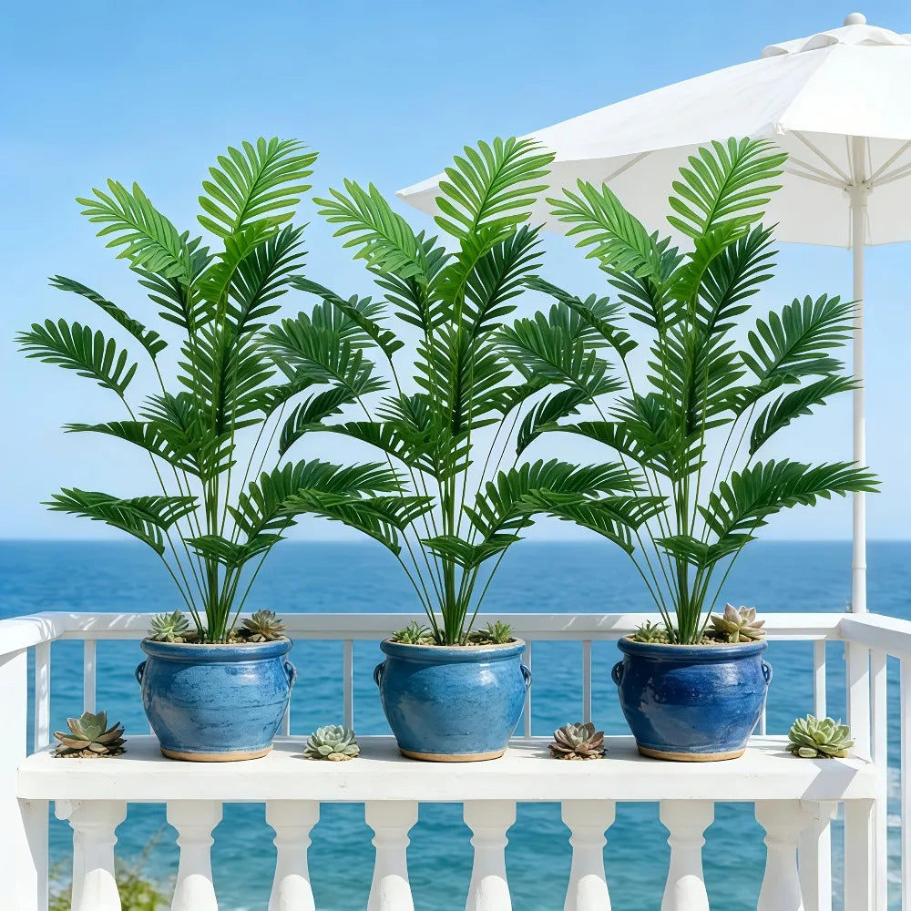 Three potted artificial palm trees with monstera leaves displayed on a white railing.