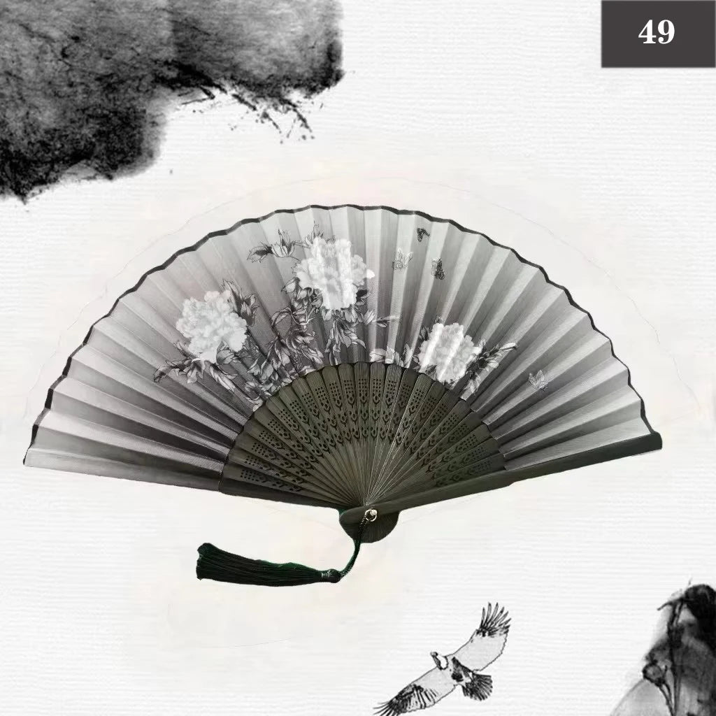 A black and white photograph of a vintage silk bamboo folding hand fan with delicate floral designs.