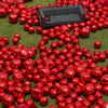 A large quantity of glossy red round foil balloons scattered on green grass with a dark gray sofa in the background.