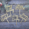 A set of elegant black and gold acrylic cake toppers with birthday messages on a weathered wooden background.
